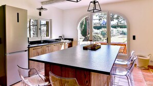 A kitchen with a large island, wooden cabinets, and a view of the garden through a large arched window.