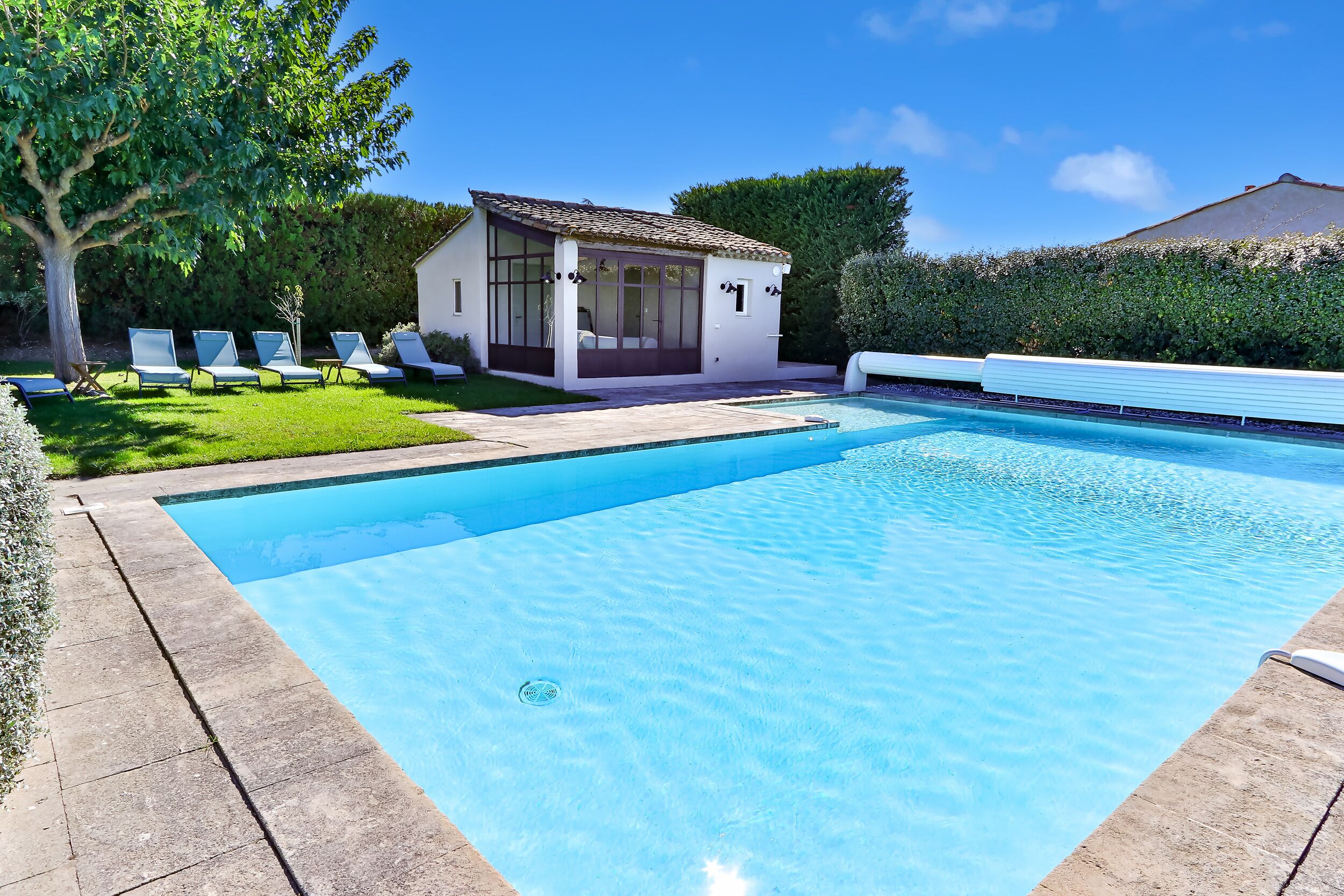 Ein Swimmingpool mit glasklarer, blauer Wasserfläche, umgeben von einem weißen Zaun und einem kleinen Gebäude mit großen Fenstern.