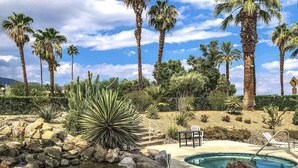 A pool area with a hot tub, surrounded by rocks and palm trees. - Hidden Gem - Spacious and Gorgeous Getaway by the Pool  (Palm Springs)