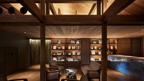 Un interior moderno con vigas de madera, un mostrador de recepción y una estantería llena de libros y cuadros.