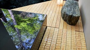 Una terraza de madera con una superficie reflectante grande y una roca.