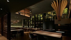 Un restaurante moderno con una barra larga, varias mesas y un amplio ventanal con vistas a zonas verdes.