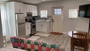 Una cocina compacta con armarios blancos, refrigerador, estufa y microondas. Hay un comedor con una mesa y sillas.