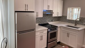 Una cocina moderna con armarios blancos, un refrigerador de acero inoxidable, una estufa y un lavamanos.