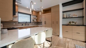Una cocina moderna con una isla grande, taburetes de bar, armarios de madera e iluminación colgante.
