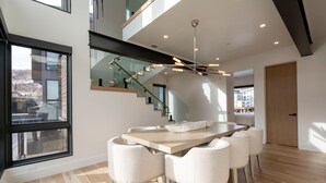Un comedor moderno con una larga mesa, seis sillas, una escalera y ventanas amplias.