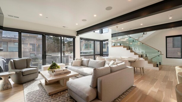 Una sala de estar moderna con un sofá modular, una mesa de centro y una escalera de cristal.