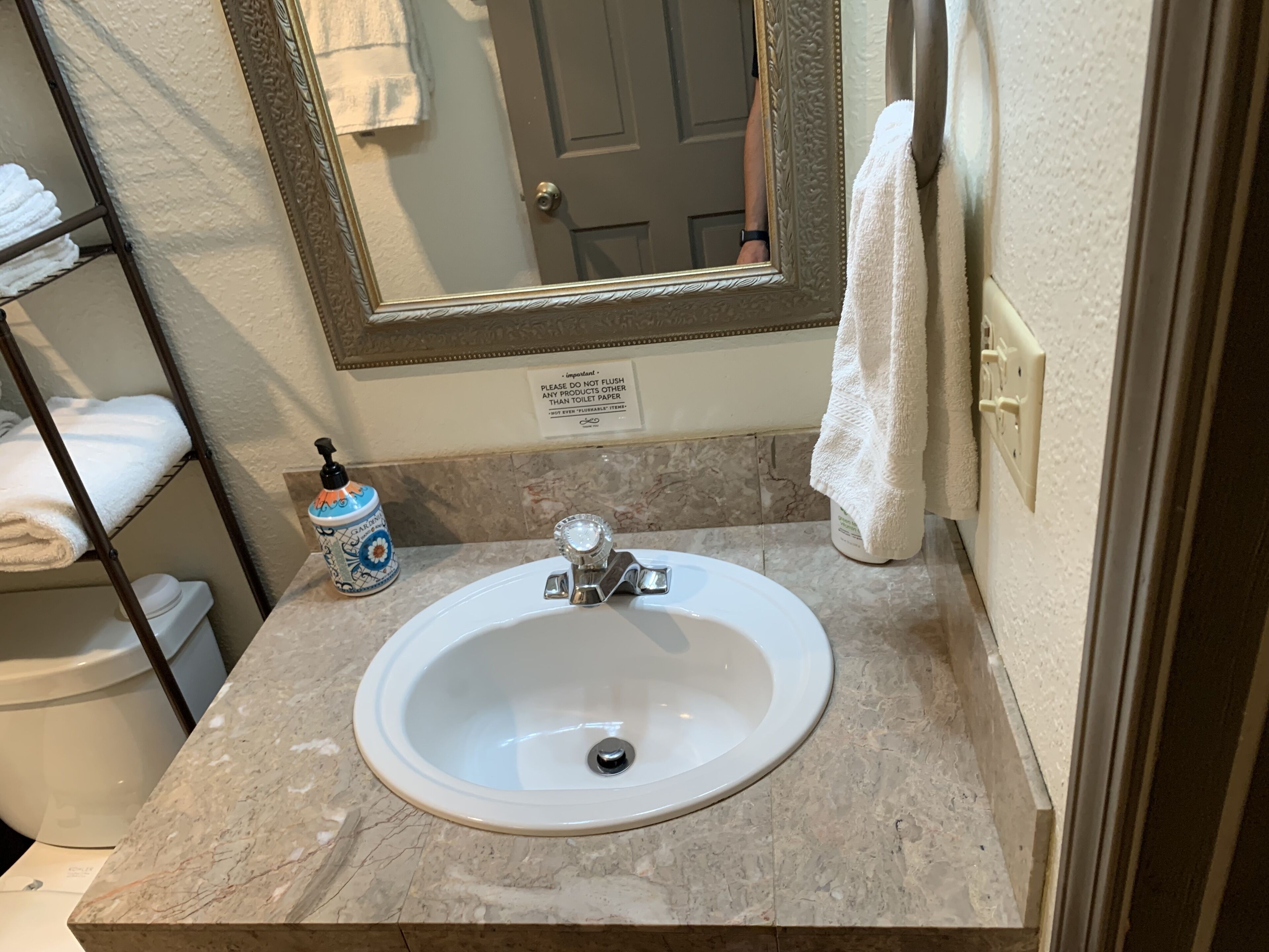 A bathroom with a marble sink, a large mirror, a towel rack, and a soap dispenser.