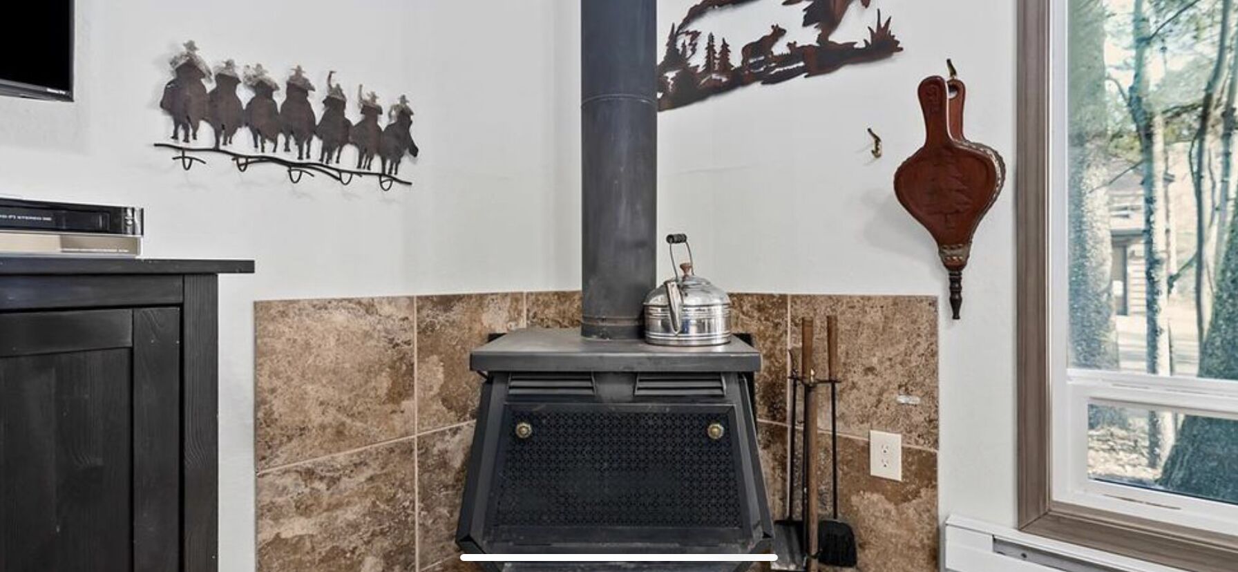 A kitchen with a wood-burning stove, decorative wall art, and a window with a view of trees.