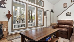 Una sala de estar con un ventanal grande, un sofá de cuero marrón, una mesa de centro de madera y una chimenea.