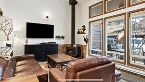 Una sala de estar con chimenea, sofá de cuero, mesa de centro de madera y un televisor grande.