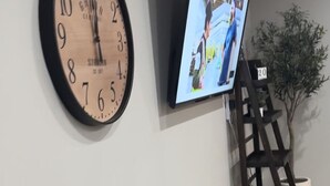 Eine Wanduhr und ein Flachbildfernseher an einer schlichten Wand.