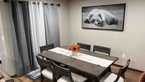 Ein Essbereich mit einem rechteckigen Tisch, sechs Stühlen, einer Vase mit orangefarbenen Blumen und einem gerahmten Bild an der Wand.