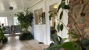 Un porche cubierto con un muro de piedra, una planta en maceta, un banco y una puerta con un cartel.