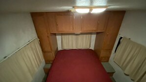 Une petite pièce avec un lit simple, des armoires en bois et des rideaux.