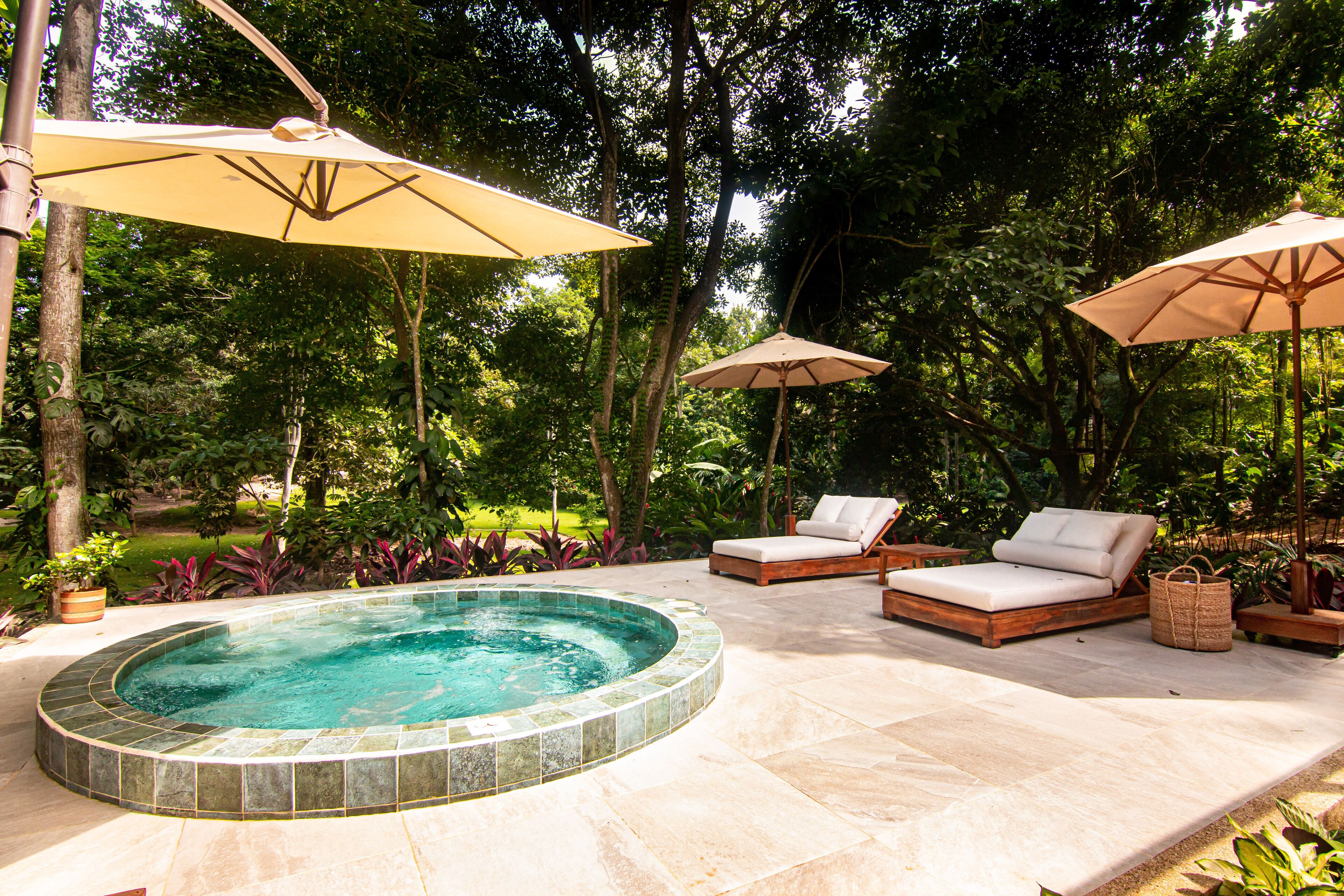 A hot tub surrounded by lounge chairs and umbrellas in a lush garden setting.
