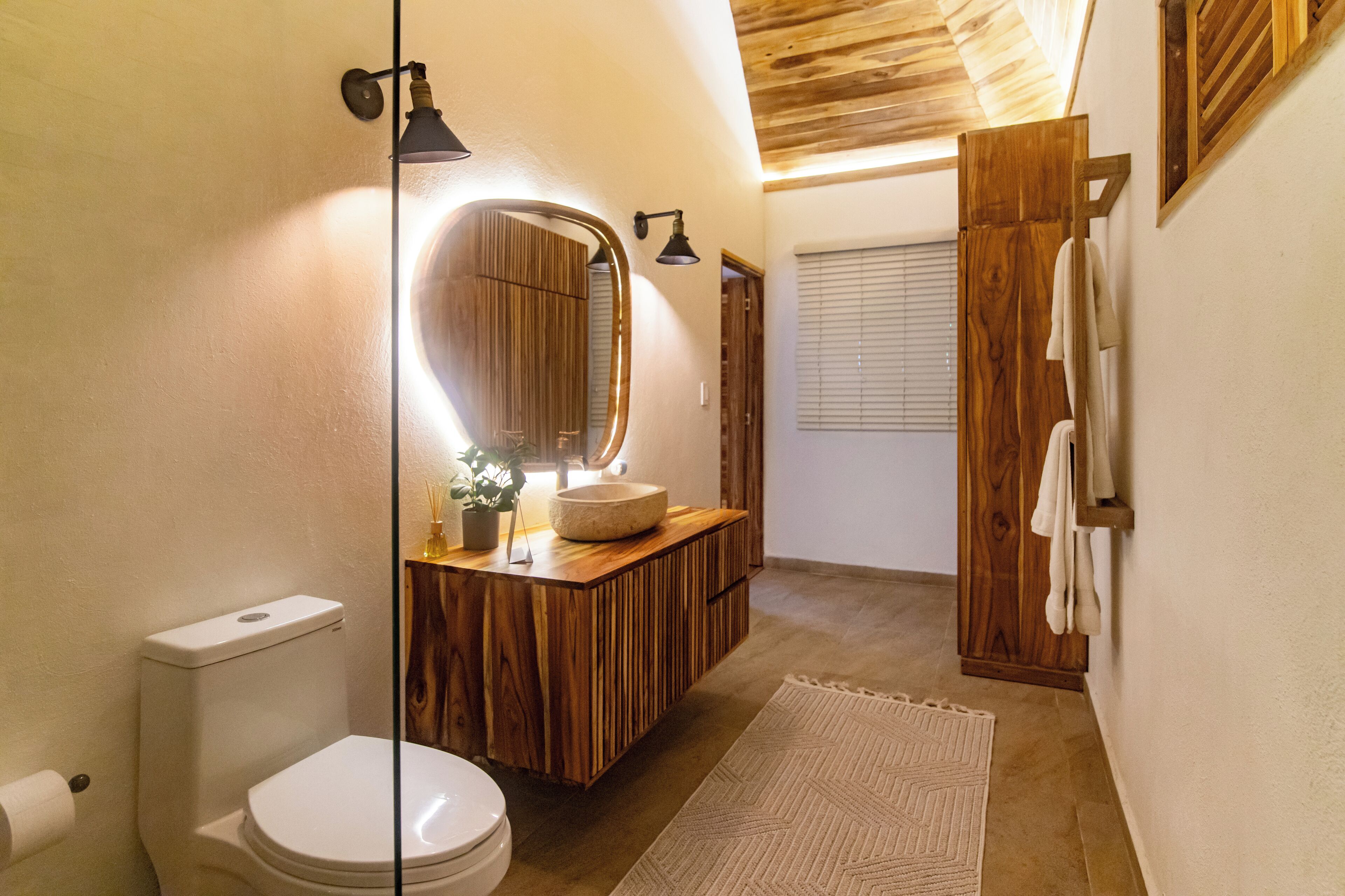 A modern bathroom with a wooden vanity, a round mirror, and a toilet.