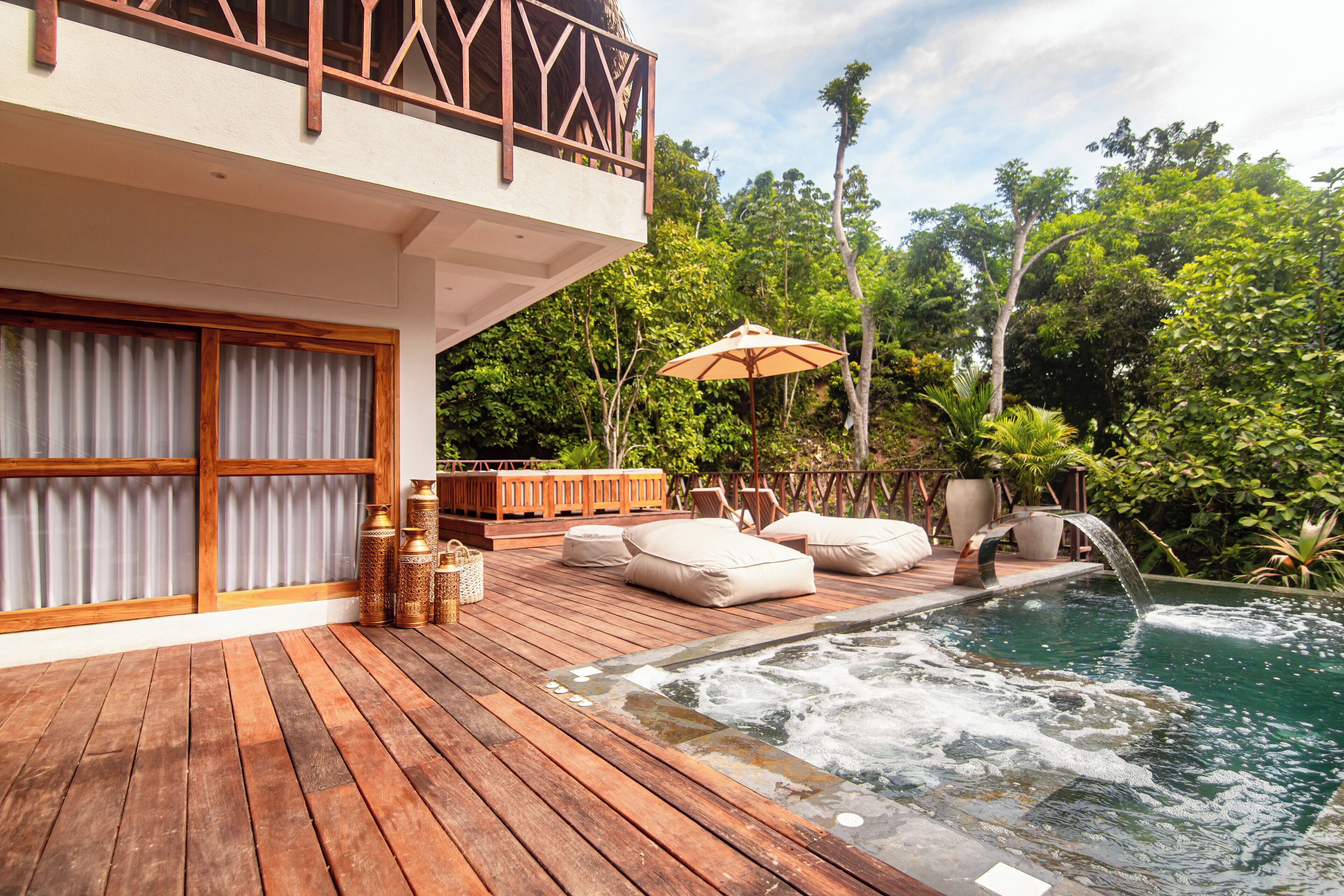 A wooden deck with a hot tub, outdoor seating, and a view of lush greenery.