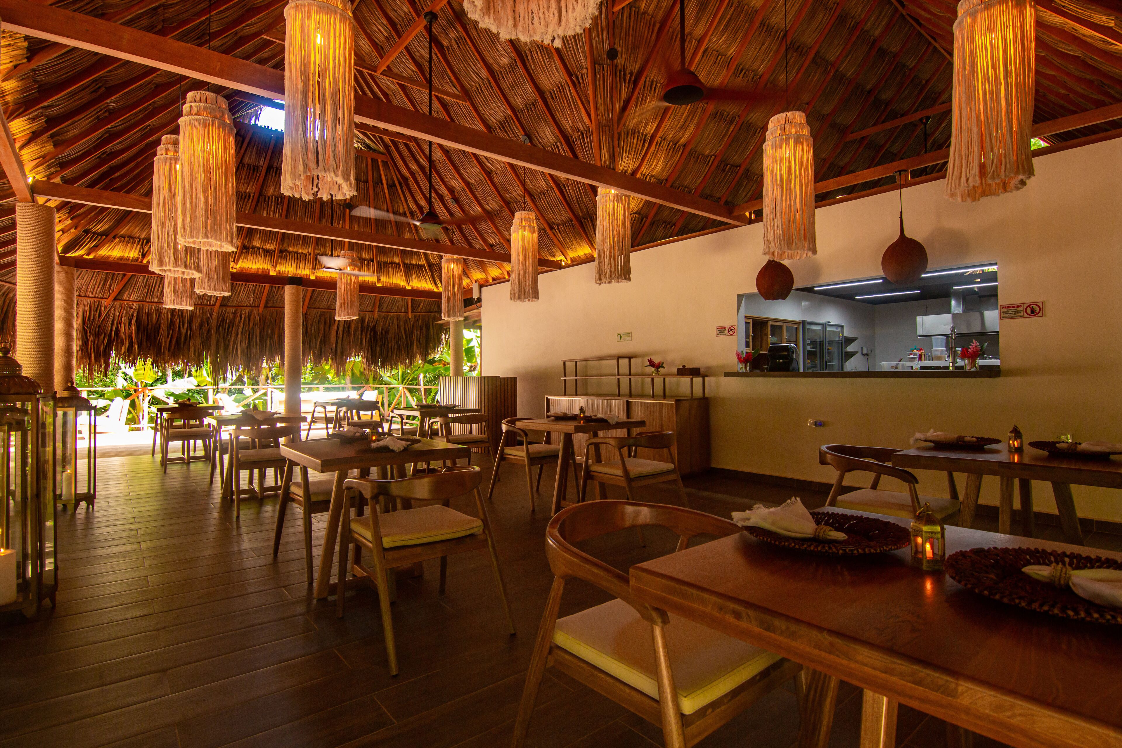 A restaurant with wooden furniture, hanging light fixtures, and a thatched roof.