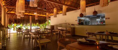 A restaurant with wooden furniture, hanging light fixtures, and a thatched roof.