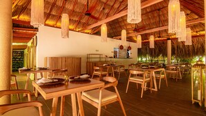 A restaurant with wooden tables and chairs, a thatched roof, and hanging light fixtures. - Tewimake Hotel  (Santa Marta)