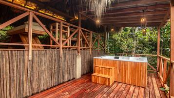 Una terraza de madera con un jacuzzi, techo de paja y valla de bambú.