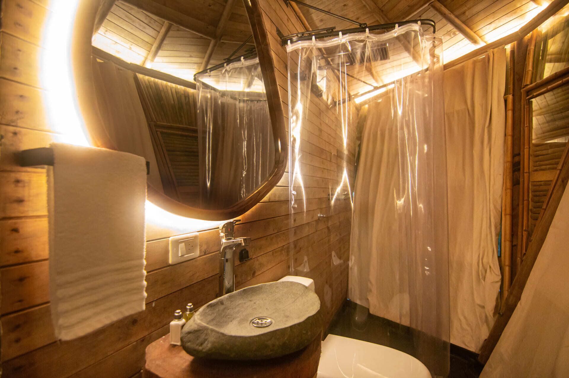 A wooden cabin bathroom with a stone sink, a mirror, and a shower curtain.