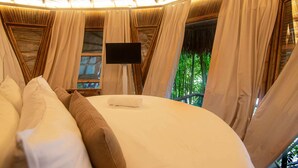 A bedroom with a bed, curtains, a TV, and a window with a view of greenery. - Tewimake Hotel  (Santa Marta)