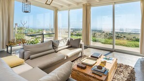 A spacious living room with a large sofa, a coffee table, and a view of a green landscape through large windows.