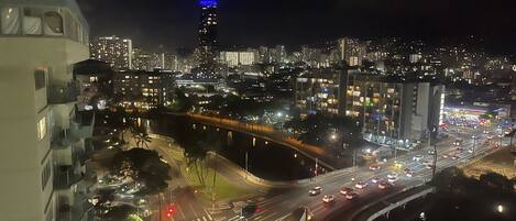A nighttime cityscape with a prominent building with blue lighting on top, a busy intersection with multiple lanes, and a river running through the city.