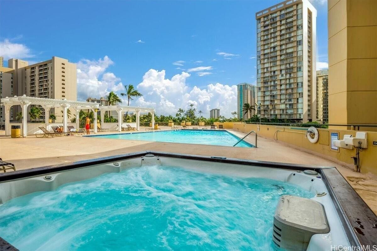 A rooftop pool area with a hot tub, lounge chairs, and a pergola.