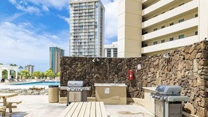 An outdoor pool area with a stone wall, a grill, and a barbecue station. - Cozy condo at Hawaiian monarch- no resort fee, free parking, near beaches, shop (Honolulu)