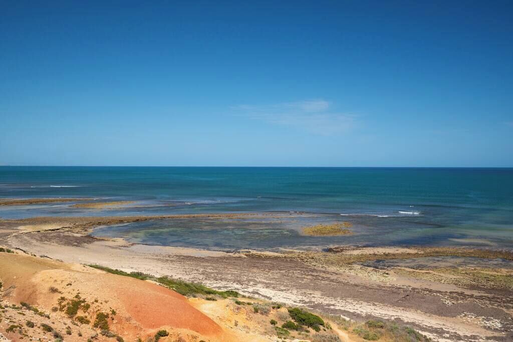A coastal landscape with a clear sky, a sandy beach, and a distant view of the ocean.