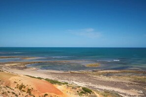 Eine Küstenlandschaft mit blauem Himmel, einem Sandstrand und einem felsigen Küstenabschnitt mit vereinzelter Vegetation.