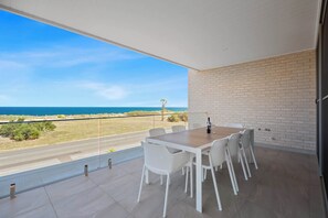 Ein Balkon mit Blick aufs Meer, einem Holztisch und weißen Stühlen.