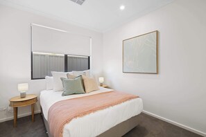 Un dormitorio con una cama, mesitas de noche, una ventana y una obra de arte colgada en la pared.