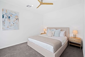 A bedroom with a bed, two bedside tables, a ceiling fan, and a wall-mounted abstract painting. - Driftwood Port Noarlunga South (Port Noarlunga South)