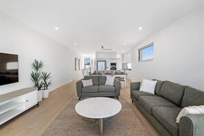 Un salon moderne avec un canapé gris, une table basse ronde et un téléviseur à écran plat posé sur un meuble blanc.