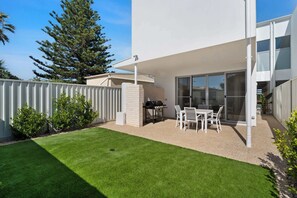 Eine moderne Terrassengrundstueck mit Grill, Sitzgelegenheiten und Blick auf das Haus.