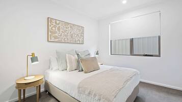 A bedroom with a bed, bedside tables, a wall-mounted radiator, and a window with blinds.