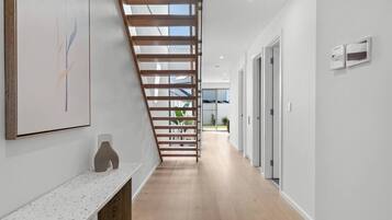 A modern interior with a wooden staircase, a white wall with a framed artwork, and a hallway leading to a door.