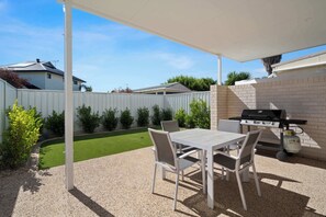 Un patio couvert avec une table et des chaises, un barbecue et une petite pelouse.