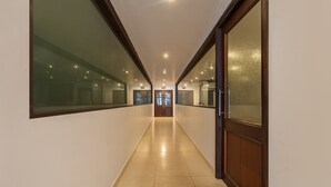 A long, narrow hallway with a tiled floor, wooden doors, and glass windows on both sides. - Treebo Central (Thrissur)
