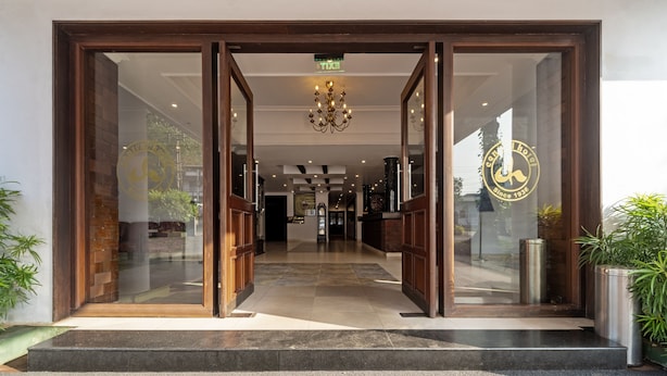 A hotel entrance with a grand wooden door, a chandelier, and a logo on the glass wall. - Treebo Central (Thrissur)