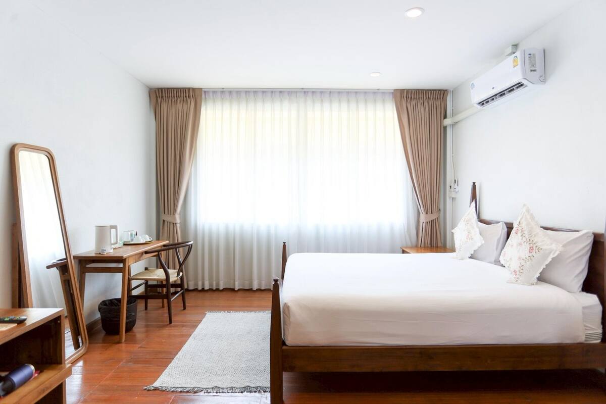 A hotel room with a bed, a desk, a chair, a mirror, and a window with curtains.