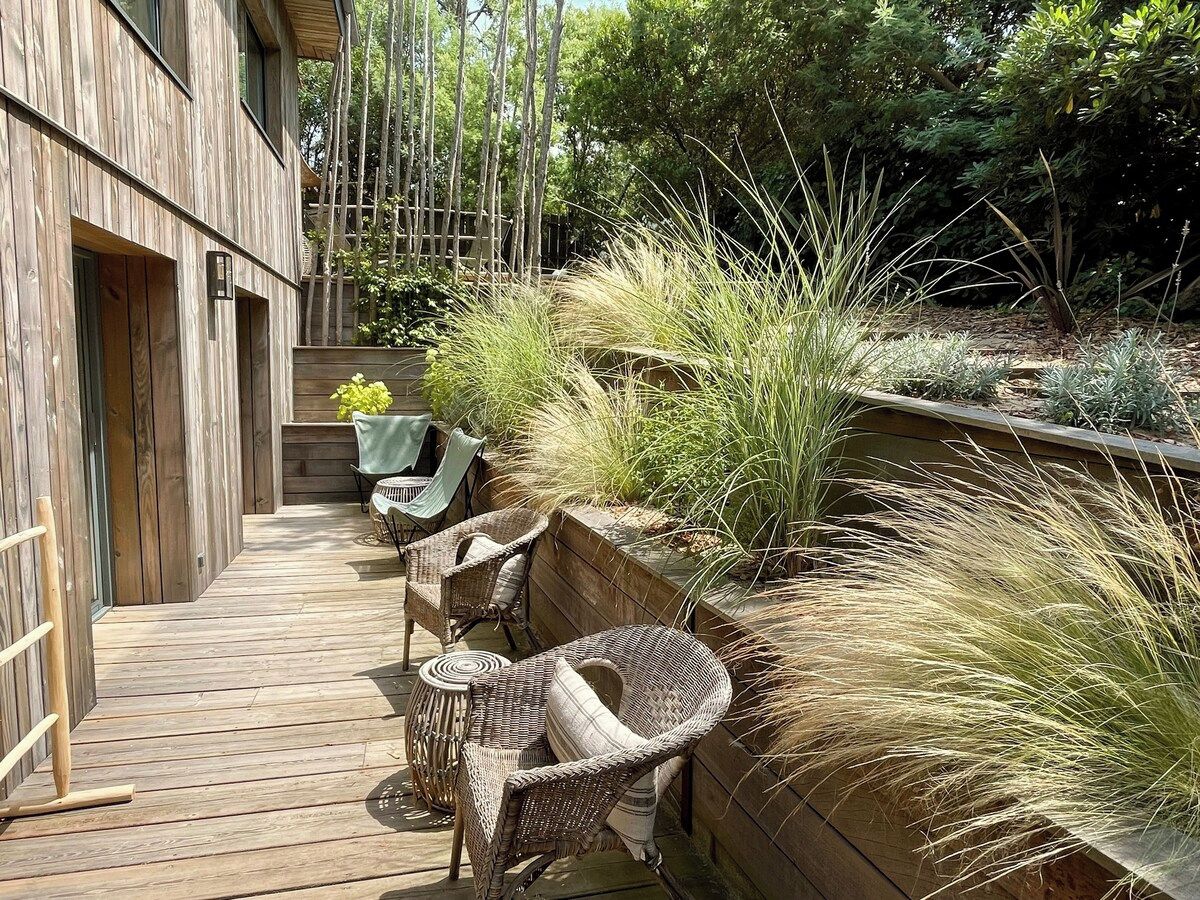 Una terraza de madera con mobiliario de mimbre y una jardinera con pastos altos.