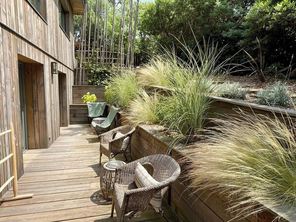 A wooden deck with wicker furniture and a planter with tall grasses.