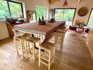 A wooden bar area with high stools and a long table, surrounded by large windows with a view of greenery. - Amazing high standard Cap Ferret Style Villa A0326 (Lège-Cap-Ferret)