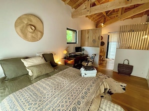 A bedroom with a bed, a desk, a chair, a window, and a hanging hat.