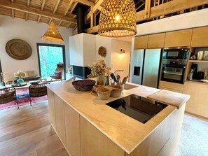Una cocina moderna con una isla central, electrodomésticos integrados y un comedor con mobiliario de mimbre.